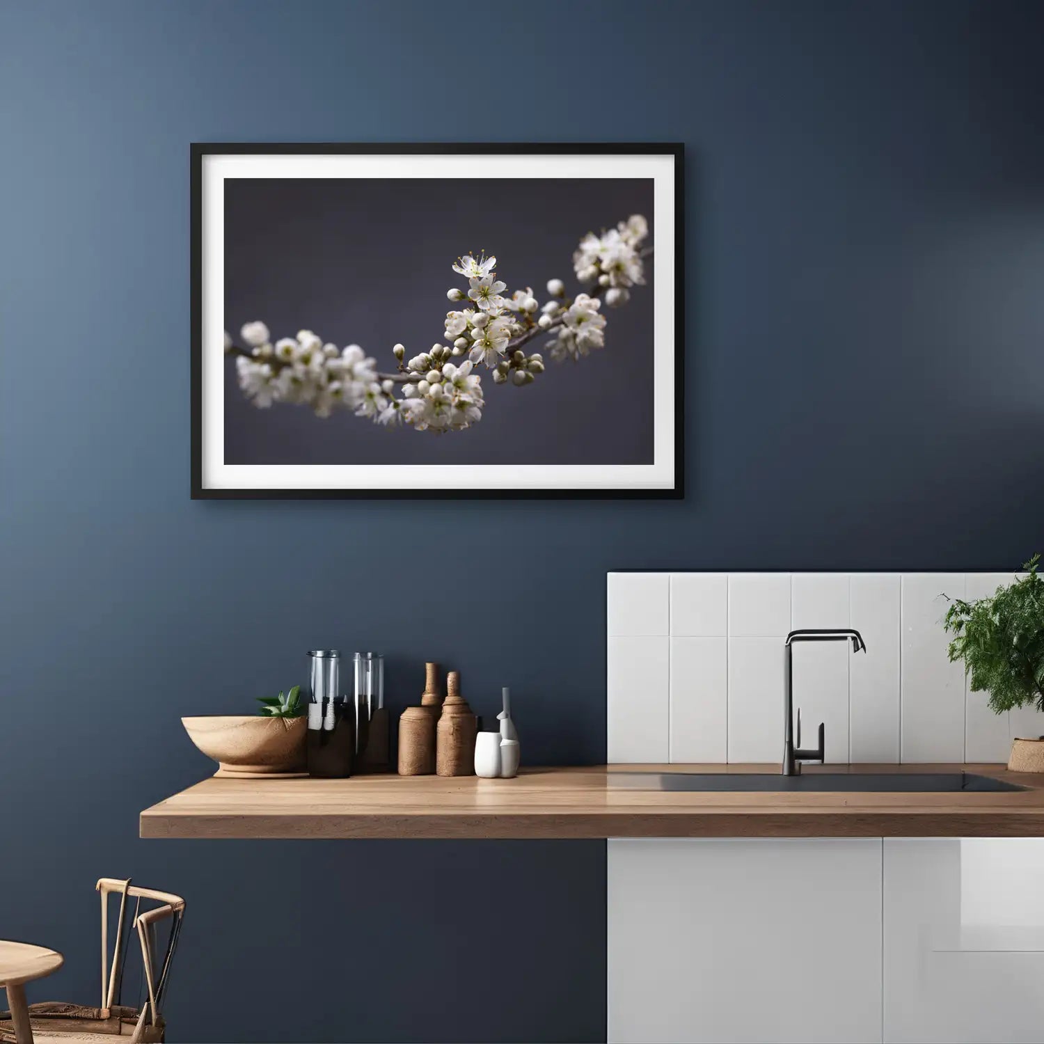 A lifestyle image for representation only showing a rich blue kitchen wall with ash coloured wood counter and white backsplash featuring a black framed blackthorn photographic print.