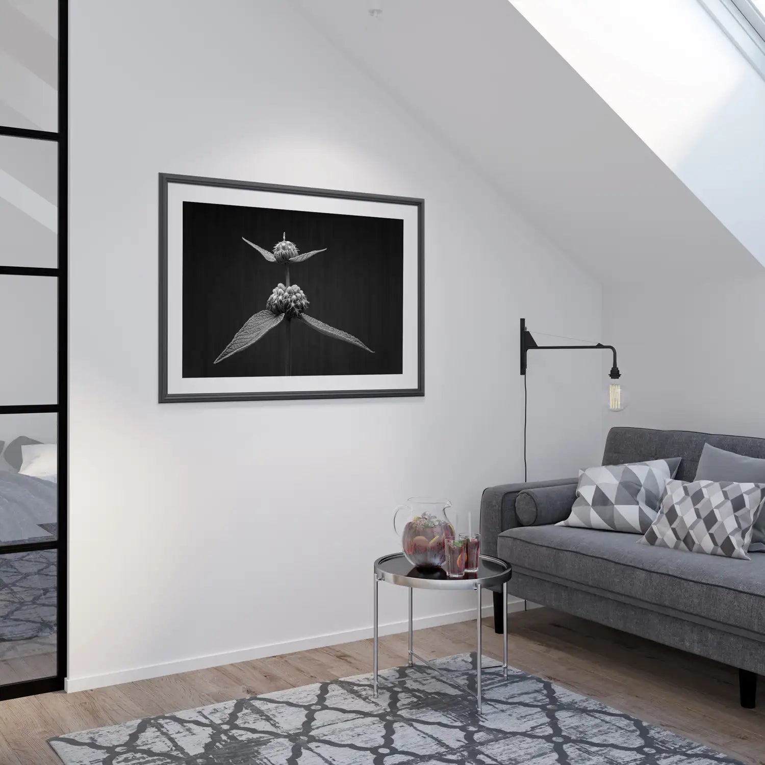 A framed black and white botanical photographic art print of two whorls of a Phlomis flowers. It sits on a naturally lit white wall in a modern, living room with a grey sofa, with grey and white cushions and a patterned rug. There is a jug of refreshments with two glasses sitting on a round silver and glass coffee table.