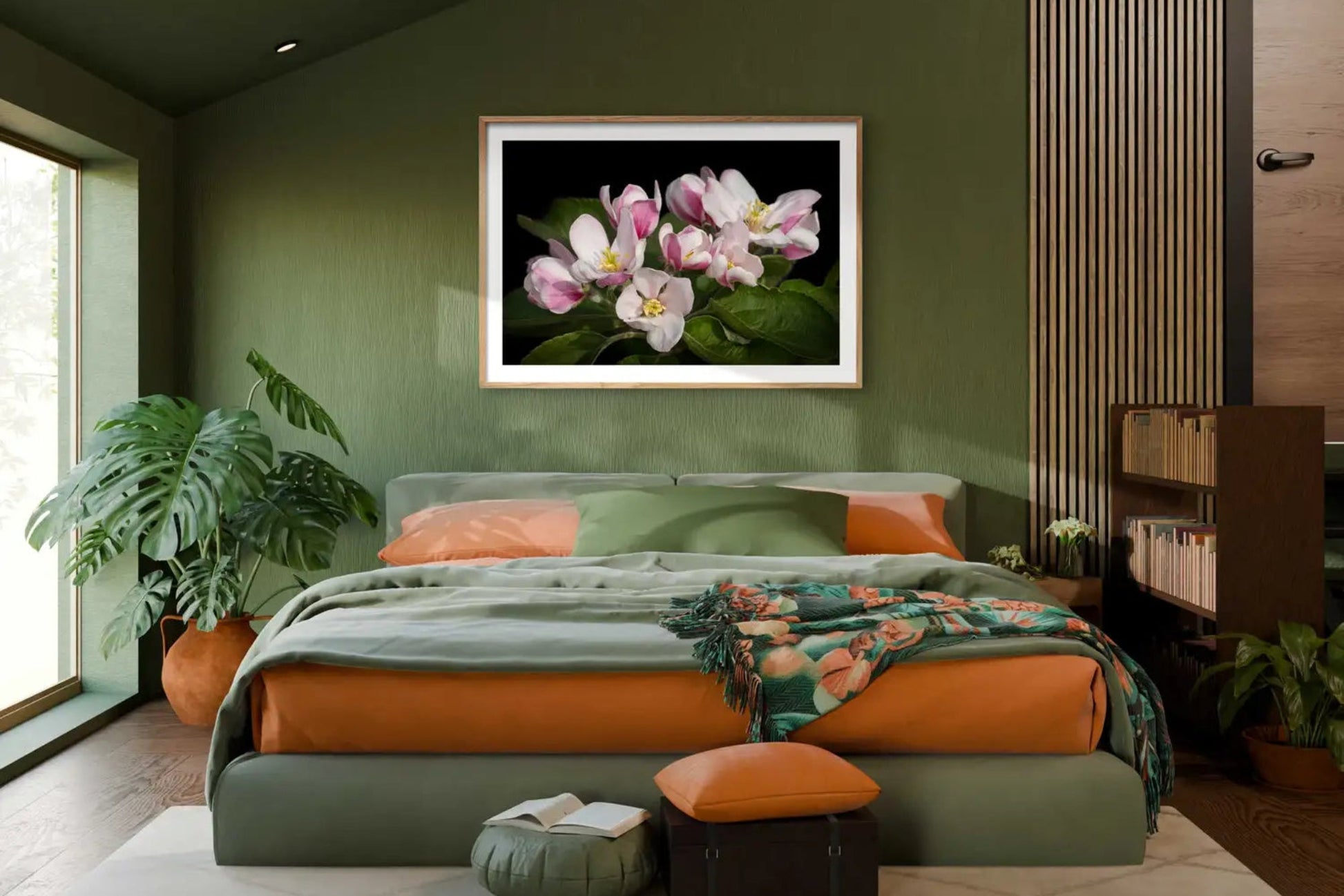 Large close up, photographic print of an apple blossom  shown in a lifestyle bedroom set of green and bright terracotta tones. Side lit from a floor length window with a beautiful broad leafed monstera plant in a rustic terracotta jar. 